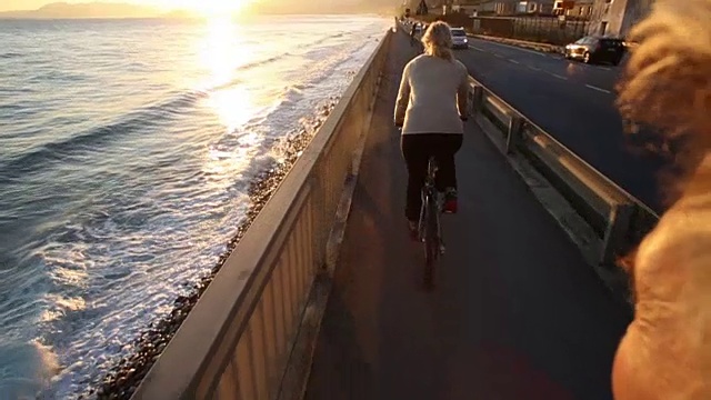 一名女子骑着自行车沿着海边的小路经过一名男子视频素材