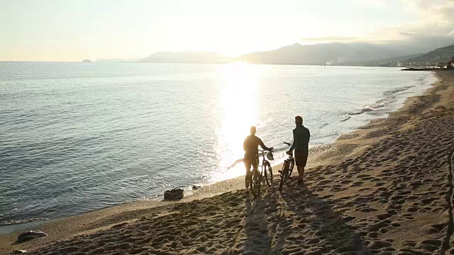 一对夫妇沿着空荡荡的海滩推着自行车，望着大海视频素材