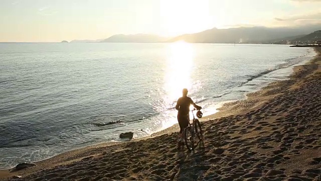 一个女人推着自行车沿着空荡荡的海滩，望着大海视频素材