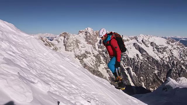 一个登山运动员在阳光下爬上陡峭的雪坡视频素材