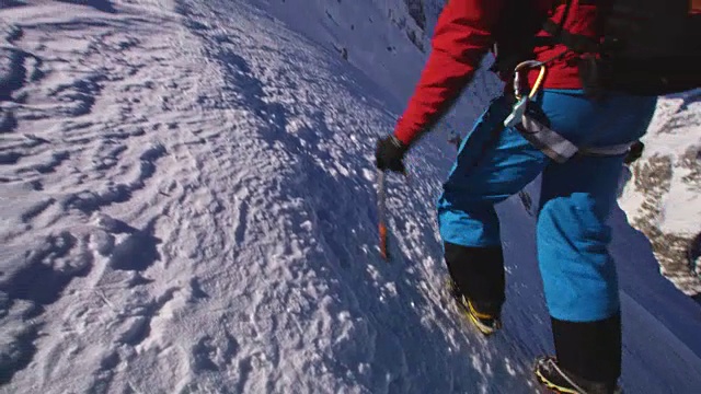 一名登山运动员在阳光下爬上白雪覆盖的山峰视频素材