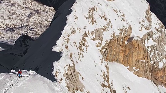 在一个阳光明媚的日子里，一名登山运动员正在穿越积雪的山脊视频素材