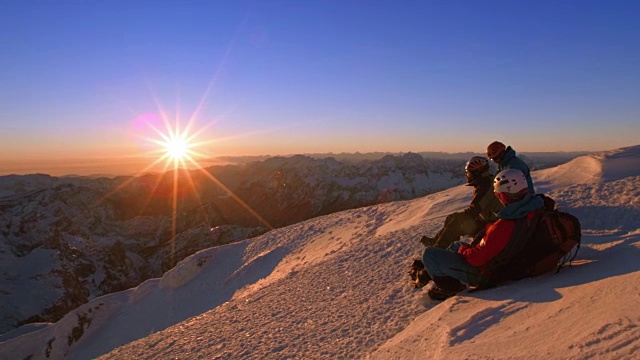 登山队员们坐在白雪皑皑的山顶上欣赏夕阳视频素材