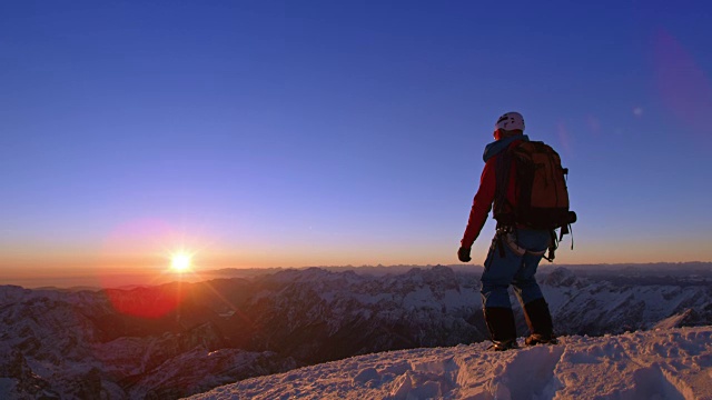 日落时分，一名登山运动员在白雪皑皑的山顶上快乐地跳跃视频素材