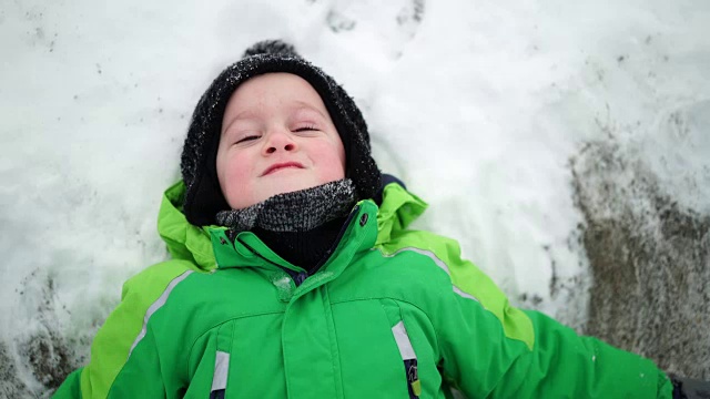 小男孩在几片雪地上做雪天使视频素材