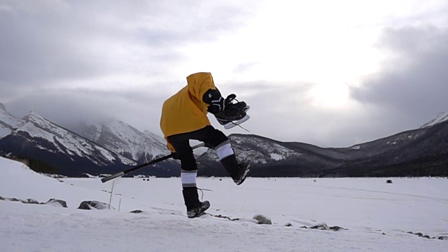 小男孩带着曲棍球装备在雪地里玩，在山上玩视频素材