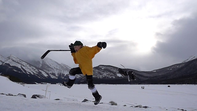 小男孩带着曲棍球装备在雪地里玩，在山上玩视频素材