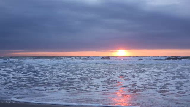 当太阳落山时，海浪撞击着海滩视频素材