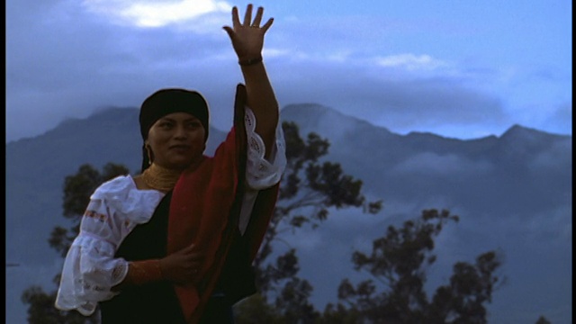 厄瓜多尔奥塔瓦洛(Otavalo)，一名身穿土著服装的女子向银幕外/背景中的山峰挥手致意视频素材