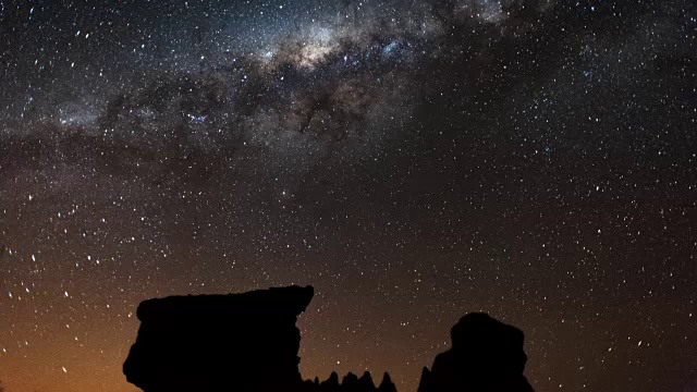 线性回拉，抽象的时间推移在夜晚的月亮落下，轮廓的侵蚀岩石形成的前景与银河系移动到框架和设置视频素材