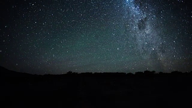 随着银河的上升和扭曲穿过天空，一些零散的云和绿色的空气辉光和陨石在夜幕降临时的线性时间流逝视频素材