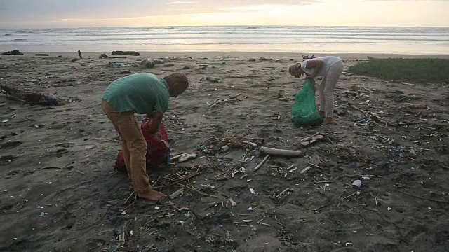 成熟的夫妇在广阔的海滩上收集垃圾，日出视频素材