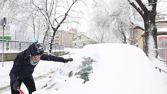 年轻女子用刷子清理车上的雪。视频素材