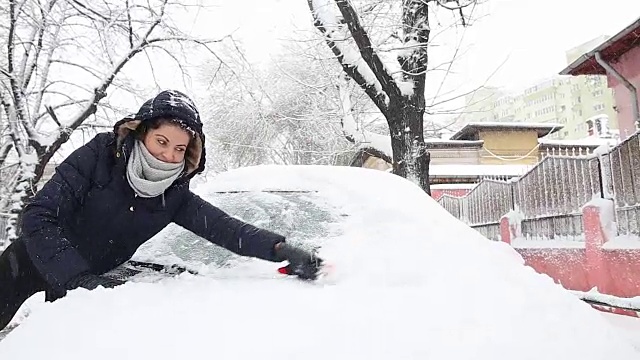 年轻女子在掸掉车上的雪。视频素材