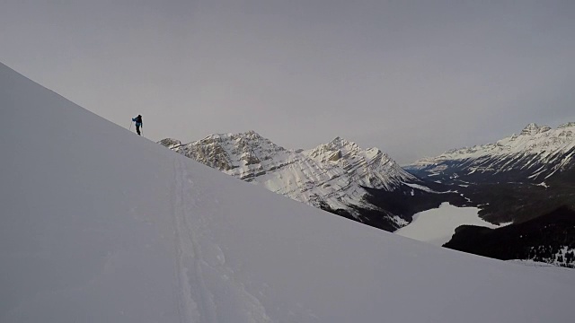 野外滑雪者使他的是沿着一个积雪的山脊和一个大的场景在他的后面视频素材