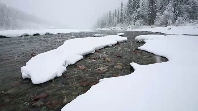 广角拍摄的河流在山上与积雪覆盖的树木和河岸覆盖在大雪暴风雪。视频素材