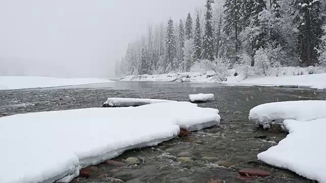 广角拍摄的河流在山上与积雪覆盖的树木和河岸覆盖在大雪暴风雪。视频素材