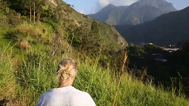 女人走在山路上，后面是火山视频素材