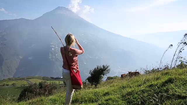 一名女子走过火山下的高山草地，用智能手机拍照视频素材