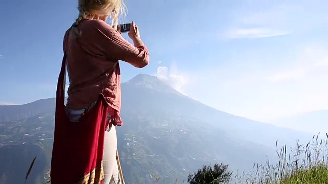 一名女子走过火山下的高山草地，用智能手机拍照视频素材