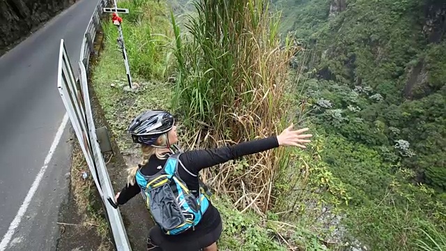 女自行车手停在绿色山谷上方的山路边视频素材