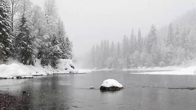 镜头右宽拍摄在大雪中，河边和山上被雪覆盖的树木。视频素材