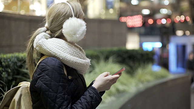 一个年轻女子在冬天的夜晚使用手机。视频素材