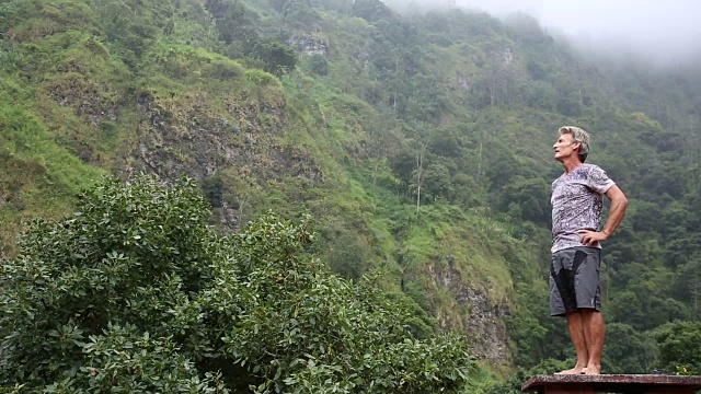 人走在热带雨林的悬崖、瀑布下，抬头仰望视频素材