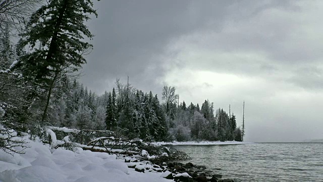 广阔的镜头，雪覆盖的海岸线上的山湖在冬天与暗灰色的云。视频素材