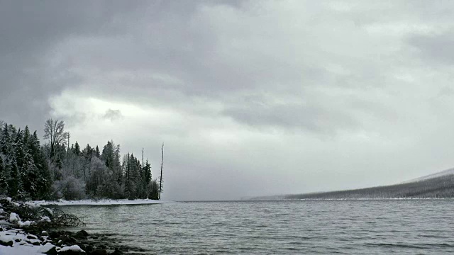 广阔的镜头，雪覆盖的海岸线上的山湖在冬天与暗灰色的云。视频素材