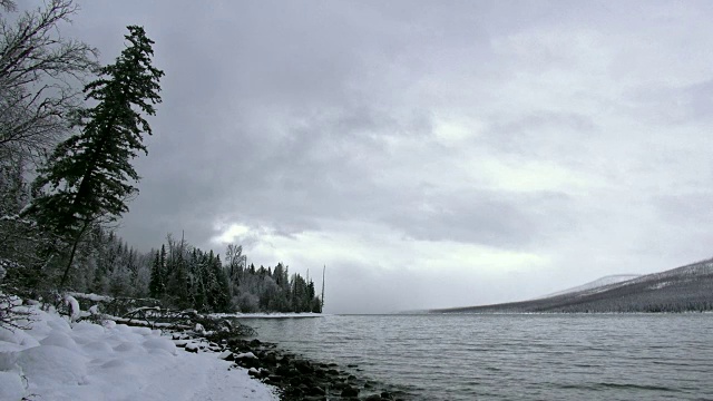 广阔的镜头，雪覆盖的海岸线上的山湖在冬天与暗灰色的云。视频素材