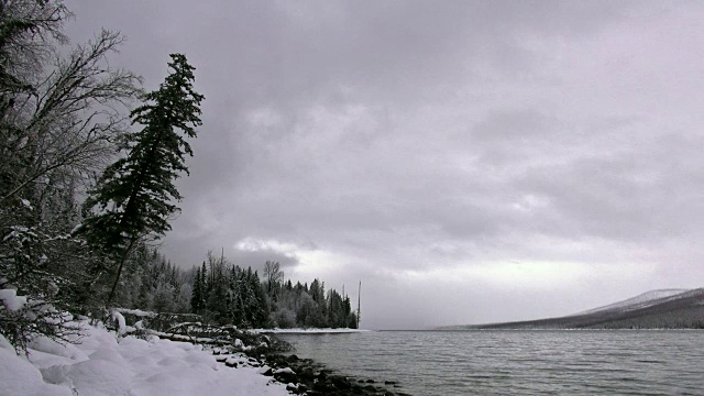 广阔的镜头，雪覆盖的海岸线上的山湖在冬天与暗灰色的云。视频素材