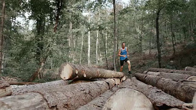 一名男性跑步者在森林里跑过一堆原木视频素材