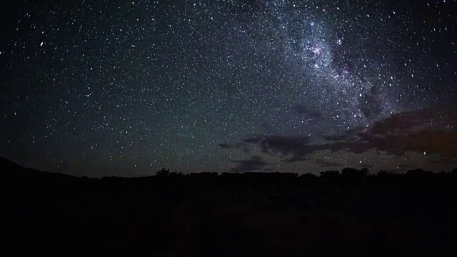 随着银河的上升和扭曲穿过天空，一些零散的云和绿色的空气辉光和陨石在夜幕降临时的线性时间流逝视频素材