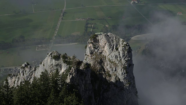 云朵在岩石山周围低低地移动，俯瞰着小村庄和风景视频素材