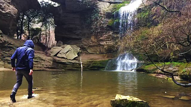 一个徒步旅行者凝视瀑布马尾在一个令人惊叹的风景与下雨的天气在一个公路旅行历险山脉的慢动作的观点。视频素材