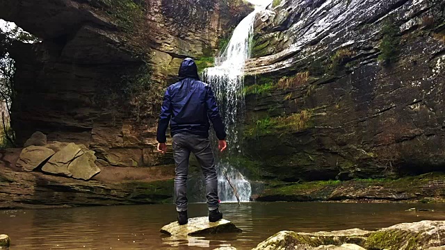 一个徒步旅行者凝视瀑布马尾在一个令人惊叹的风景与下雨的天气在一个公路旅行历险山脉的慢动作的观点。视频素材