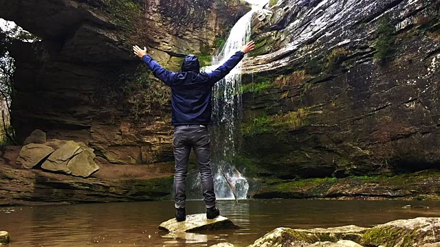 一个徒步旅行者凝视瀑布马尾在一个令人惊叹的风景与下雨的天气在一个公路旅行历险山脉的慢动作的观点。视频素材