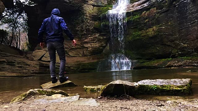 一个徒步旅行者凝视瀑布马尾在一个令人惊叹的风景与下雨的天气在一个公路旅行历险山脉的慢动作的观点。视频素材