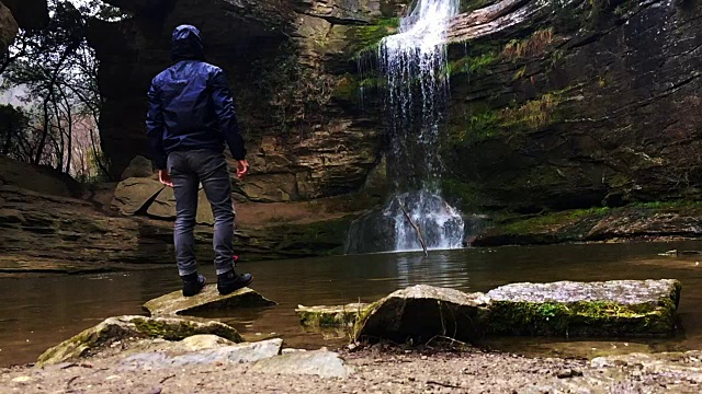 一个徒步旅行者凝视瀑布马尾在一个令人惊叹的风景与下雨的天气在一个公路旅行历险山脉的慢动作的观点。视频素材