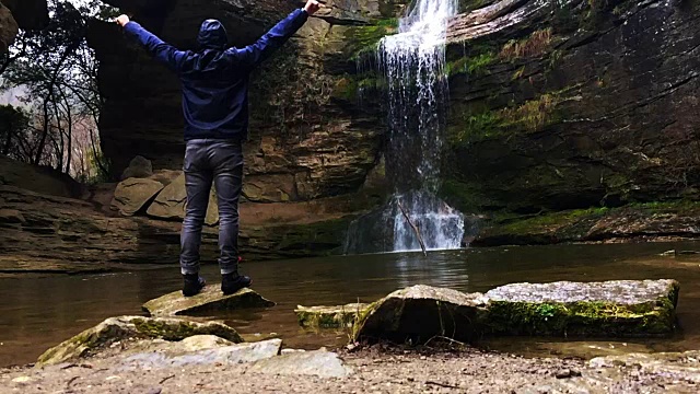 一个徒步旅行者凝视瀑布马尾在一个令人惊叹的风景与下雨的天气在一个公路旅行历险山脉的慢动作的观点。视频素材