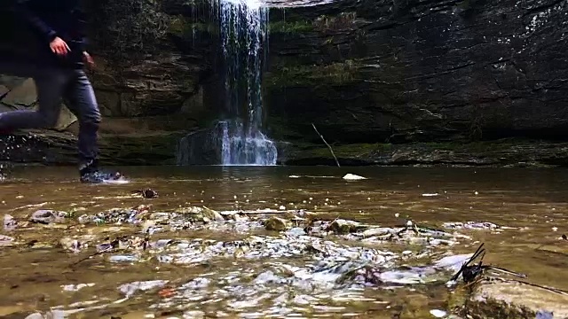 一个徒步旅行者在瀑布马尾池溅水在一个令人惊叹的风景与下雨的天气在一个公路旅行冒险通过山脉的慢动作视图。视频素材