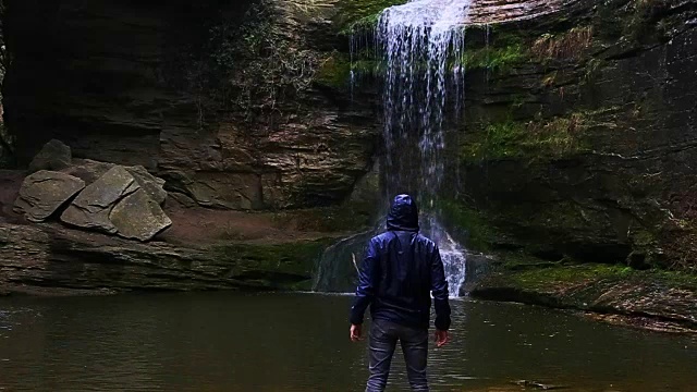 一个徒步旅行者凝视瀑布马尾在一个令人惊叹的风景与下雨的天气在一个公路旅行历险山脉的慢动作的观点。视频素材