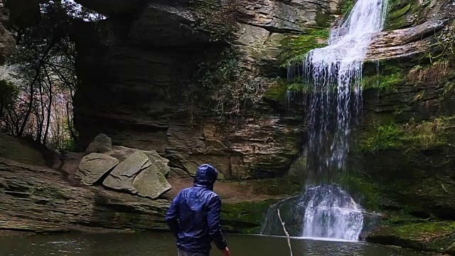 一个徒步旅行者凝视瀑布马尾在一个令人惊叹的风景与下雨的天气在一个公路旅行历险山脉的慢动作的观点。视频素材