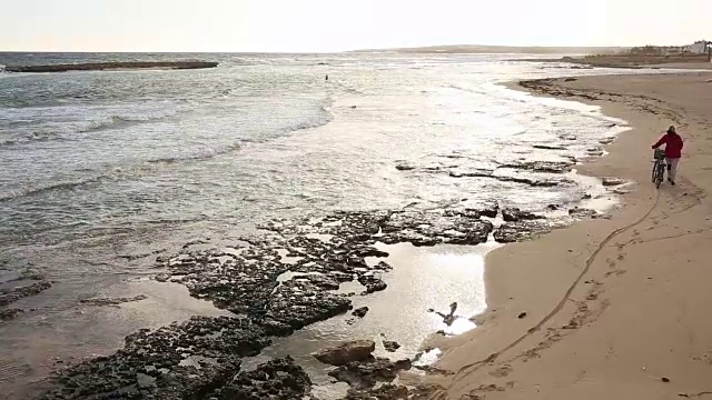 女人推着自行车沿着空荡荡的海滩，旁边是冲浪板视频素材