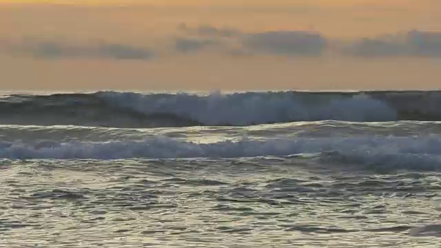 低角度的银色海洋，波浪与橙色的天空和蓝色的云在地平线上，鸟飞翔视频素材