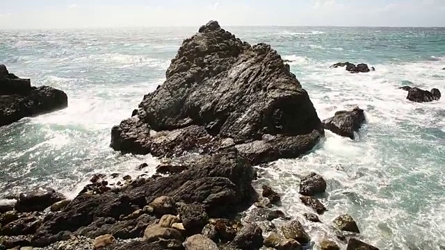 大苏尔的岩石海岸线，海浪拍打着海岸，阳光照耀着。视频素材