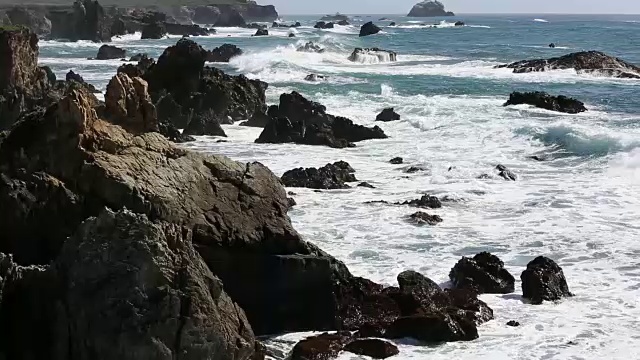 大苏尔的岩石海岸线，海浪拍打着海岸，阳光照耀着。视频素材