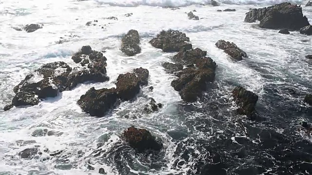 大苏尔的岩石海岸线，海浪拍打着海岸，阳光照耀着。视频素材