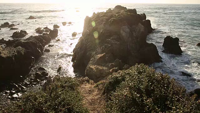 大苏尔的岩石海岸线，海浪拍打着海岸，阳光照耀着。视频素材